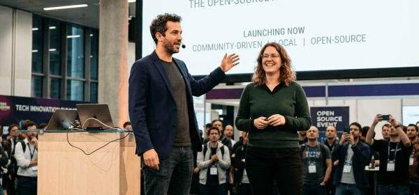Two people speaking on stage at an event with a large OLLAMA AI platform launch screen behind them