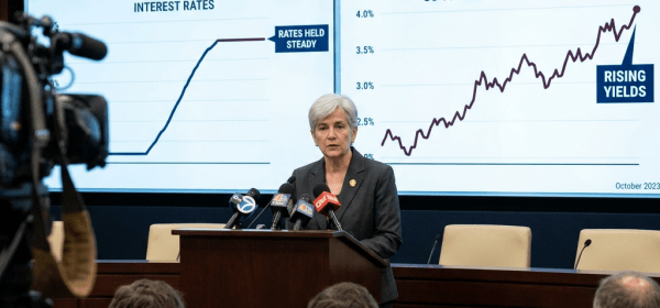 Federal Reserve official speaking in front of charts on interest rates and treasury yields at a press conference