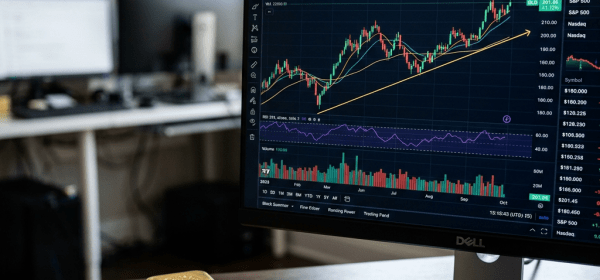 Computer monitor showing Gold ETF performance chart with upward trend lines and physical gold bars on desk